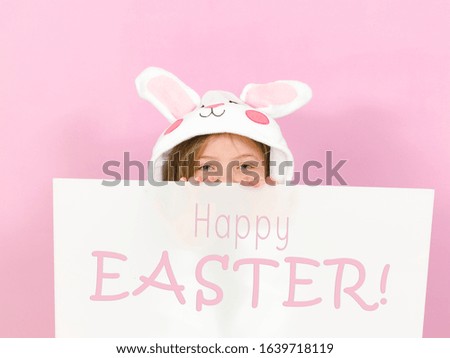 pretty blonde girl with cozy rabbit costume and white sign with the words happy easter on it is posing in the studio and is happy