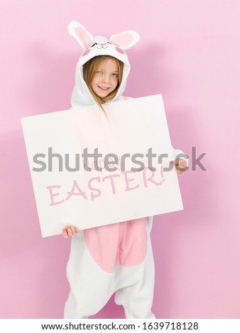 pretty blonde girl with cozy rabbit costume and white sign with the words happy easter on it is posing in the studio and is happy