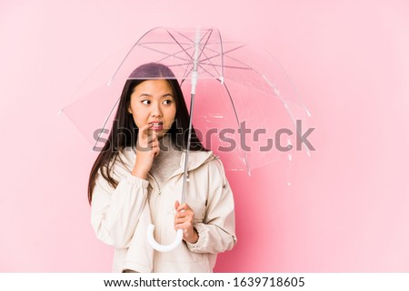 Young chinese woman holding a umbrella isolated relaxed thinking about something looking at a copy space.