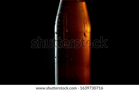 Close up cold beer in a misted glass bottle on a black background. Drops of water flowing down. A ray of light beautifully illuminates it. Craft beer closeup