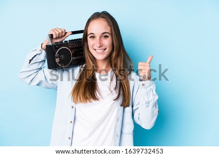 Young caucasian woman holding a cassete isolated smiling and raising thumb up