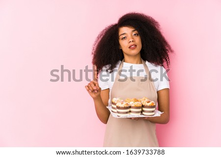Young afro pastry maker woman holding a cupcakes isolatedYoung afro baker woman showing number one with finger.
