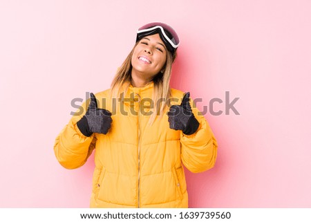Young caucasian woman wearing a ski clothes in a pink background raising both thumbs up, smiling and confident.