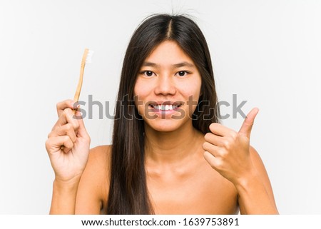Young chinese woman holding a teeth brush isolated smiling and raising thumb up