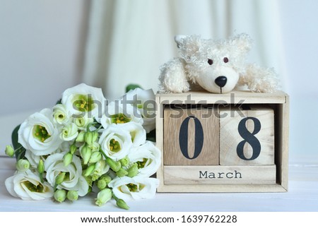 March 8 text on wooden block calendar and white eustomas and bear.Greeting card with white eustomas.Spring card template. Women's Day. Greeting card for mother's day. Copy space. Selective focus
