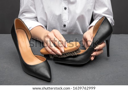 Leather shoes care concept. Shoe cleaning and polishing background with free copy space. Woman in white shirt cleaning her black leather shoes closeup Royalty-Free Stock Photo #1639762999