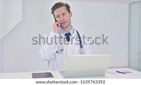 Young Doctor Talking on Smartphone in Clinic 