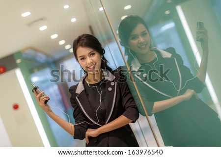 Women suits are standing listening to music. of smart phone happy in the office. Royalty-Free Stock Photo #163976540