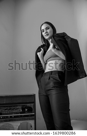 a beautiful Caucasian young woman in a black pantsuit and black sandals poses next to a vintage record player with a gramophone record in her hands. black and white picture