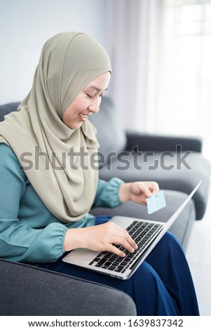 Female muslim woman using laptop while holding credit card.