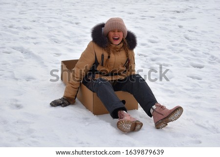 Girl riding snow hill. Slip in box in mountains. Fun winter games. Sports winter. Funny photo of child. Girl in box on snow. Winter sports holidays. Happy child in Christmas. Happy kid in box autdoor.