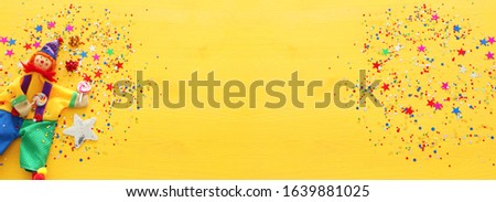 Party colorful noisemaker and cute clown over yellow wooden background . Top view, flat lay