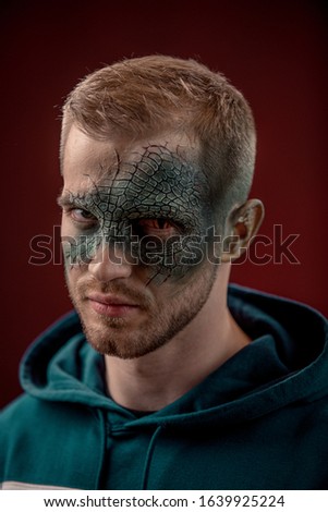 man with professional horror movie make-up green lizard on dark red background. lizard eye
