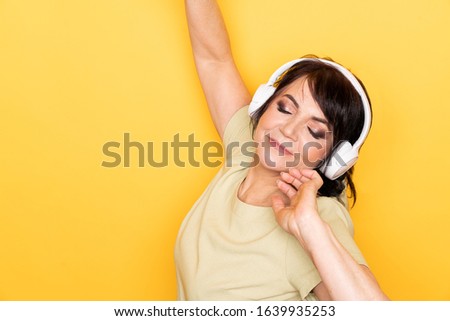Beautiful Senior woman dancing and relaxing in the wireless headphones over yellow background. Indoor