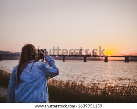 backside of hipster woman photographer during setting and take photo by her camera to beautiful bridge and river during sunset background