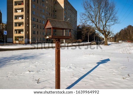Wooden birdfeeder at the road with view of living block in a sunny winter day. Balashikha, Russia.