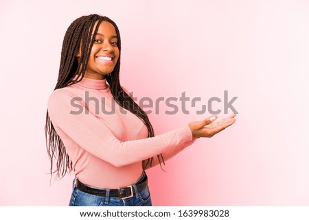 Young african american woman isolated on a pink background holding a copy space on a palm.