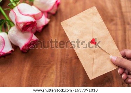 Happy Valentine's Day background with copy space. Female hand holding love letter with pink rose bouquet on a wooden surface concept for anniversary, couple love, propose, pamphlet, cover.