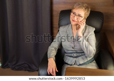 adult woman with a short haircut in a suit sits in the chair of a private plane with a phone in her hands