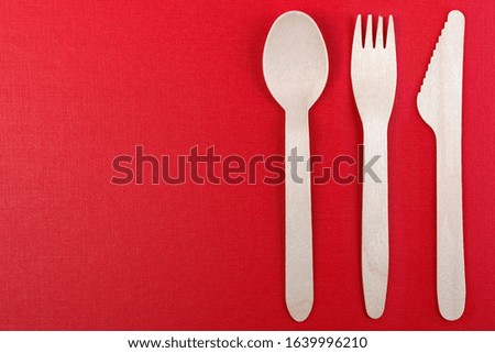 Wooden, disposable tableware on a red background. Eco-friendly materials.