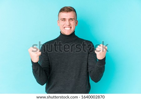 Young caucasian man on a blue background cheering carefree and excited. Victory concept.