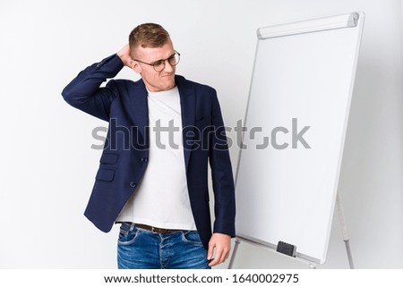 Young coaching man showing a white board touching back of head, thinking and making a choice.