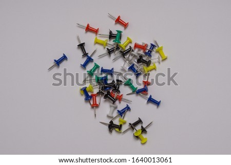 Thumbtacks of different bright colors are scattered randomly on a gray background.