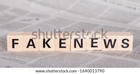 fakenews text on wooden cubes, newspaper as background Royalty-Free Stock Photo #1640013790