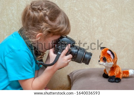 
A little girl photographs a children's toy with a reflex camera.