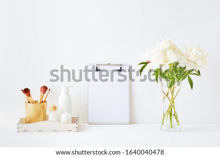 Home interior with decor elements. Mockup clipboard, white peonies in a vase, cosmetic set