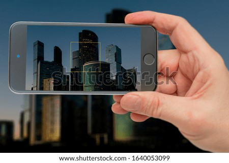 Buildings on smartphone screen. Skyscrapers in sunset light. Lights of night city.