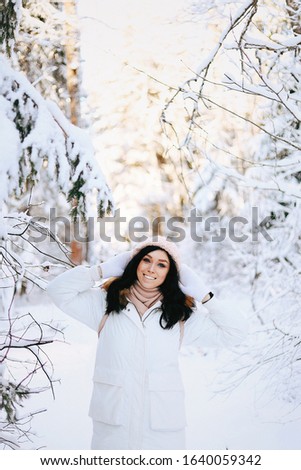 Outdoor portrait of fascinating brunette lady posing with romantic smile on snowy background. Photo of pretty laughing girl in knitted hat and soft sweater on the winter street.