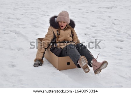 Girl riding snow hill. Slip in box in mountains. Fun winter games. Sports winter. Funny photo of child. Girl in box on snow. Winter sports holidays. Happy child in Christmas. Happy kid in box autdoor.