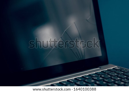 The screen laptop cracked and damaged. A silver laptop with a broken tablet with a cracked display. A close-up picture of part of broken laptop and cracked screen on a classic blue background