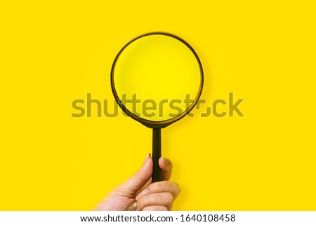 hand holding magnifier over yellow background