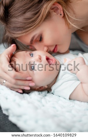 Portrait of beautiful mother with newborn baby indoor. Three month baby lying on cozy blanket. Happiness wor woman to be near her love infant