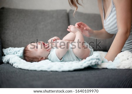 Mother touches baby legs on arms. Mom kisses the 3 month kid tender little heels. people dressed fashion home clothes