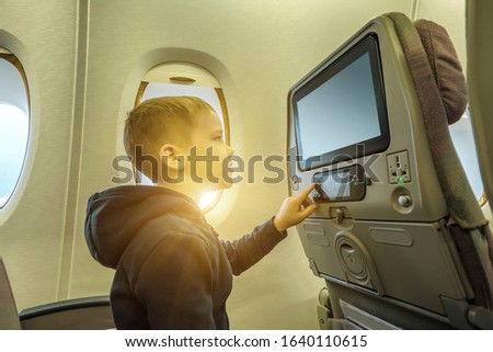 Adorable little boy traveling by airplane. Child sitting by aircraft window and looking on monitor. Traveling abroad with kids.