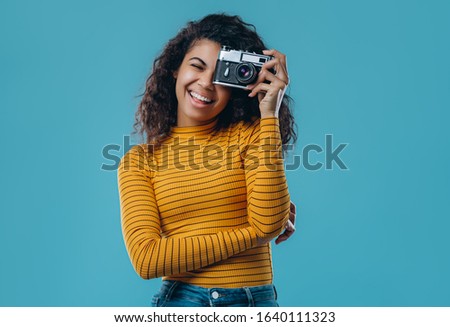 Beautiful African American girl makes a photo on a retro camera isolated on a blue background.