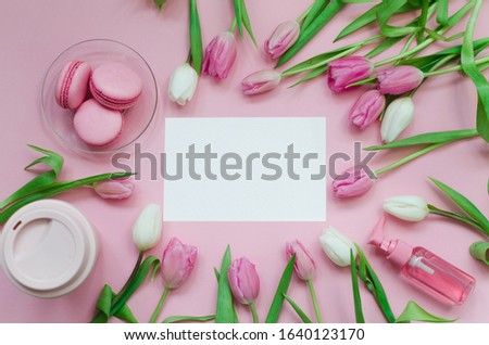 White picture, coffee cup, spring tulip flowers and pink macarons on pastel table top view. Greeting for Womans or Mothers Day. Flat lay.