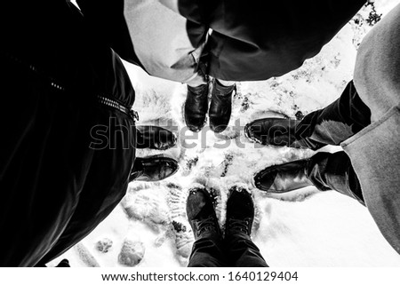 In the photo, the legs of four people standing in a circle. Black and white photo.