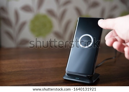smartphone wireless charging on charging stand on wooden table. male hand placing phone to charging