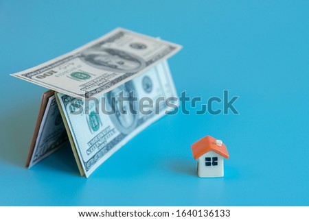 depicts saving for a house or flat manageable. Mortgage concept. house figurine and house made of dollars on a blue background