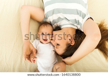 Top view of a happy mother kissing a baby lying on a bed.