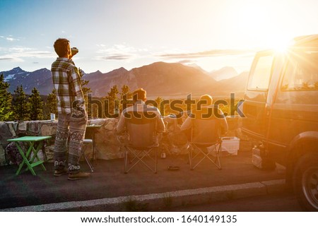 Group of three friends makes van picnic at car in Waterton National Park, Alberta, Canada. Golden sunset backlight evening photo. Hiker taking a brake rest after demanding day in mountain terrain.