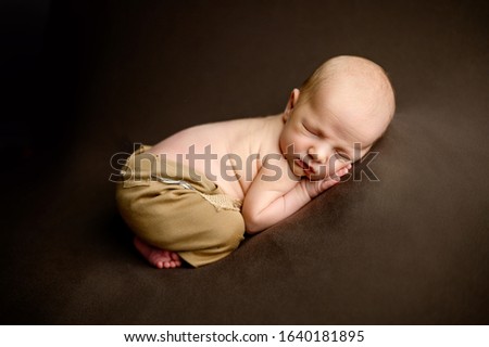Lovely newborn baby boy sleaping toshie up pose an bean bag dressed in brown pants