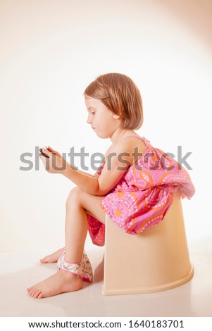 Social media mania addiction concept. Portrait of little child girl with phones sitting on toilet bowl.