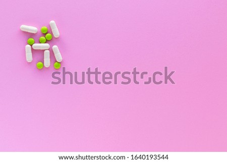 Green pills and white capsules isolated on pink background. Woman health. Pharmaceutical industry. Epidemic, painkillers, healthcare and treatment concept. Flat lay. Top view with copy space.