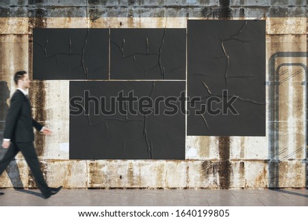 Businessman walking near blank three black billboards on loft style concrete wall. Presentation concept.