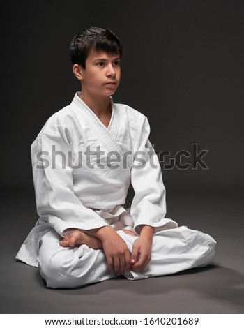 portrait of a teenager dressed in martial arts clothing poses on a dark gray background, a sports concept